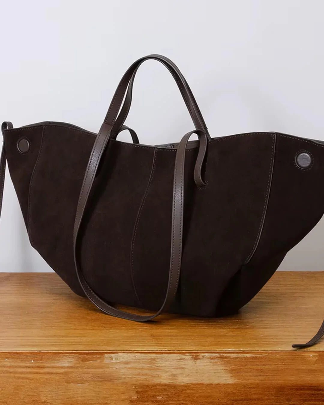 Brown suede tote bag with leather handles on wooden surface