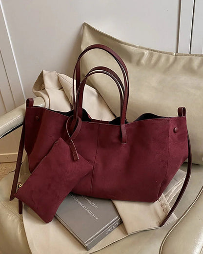 Burgundy suede tote bag with matching pouch on a beige chair, elegant and spacious design