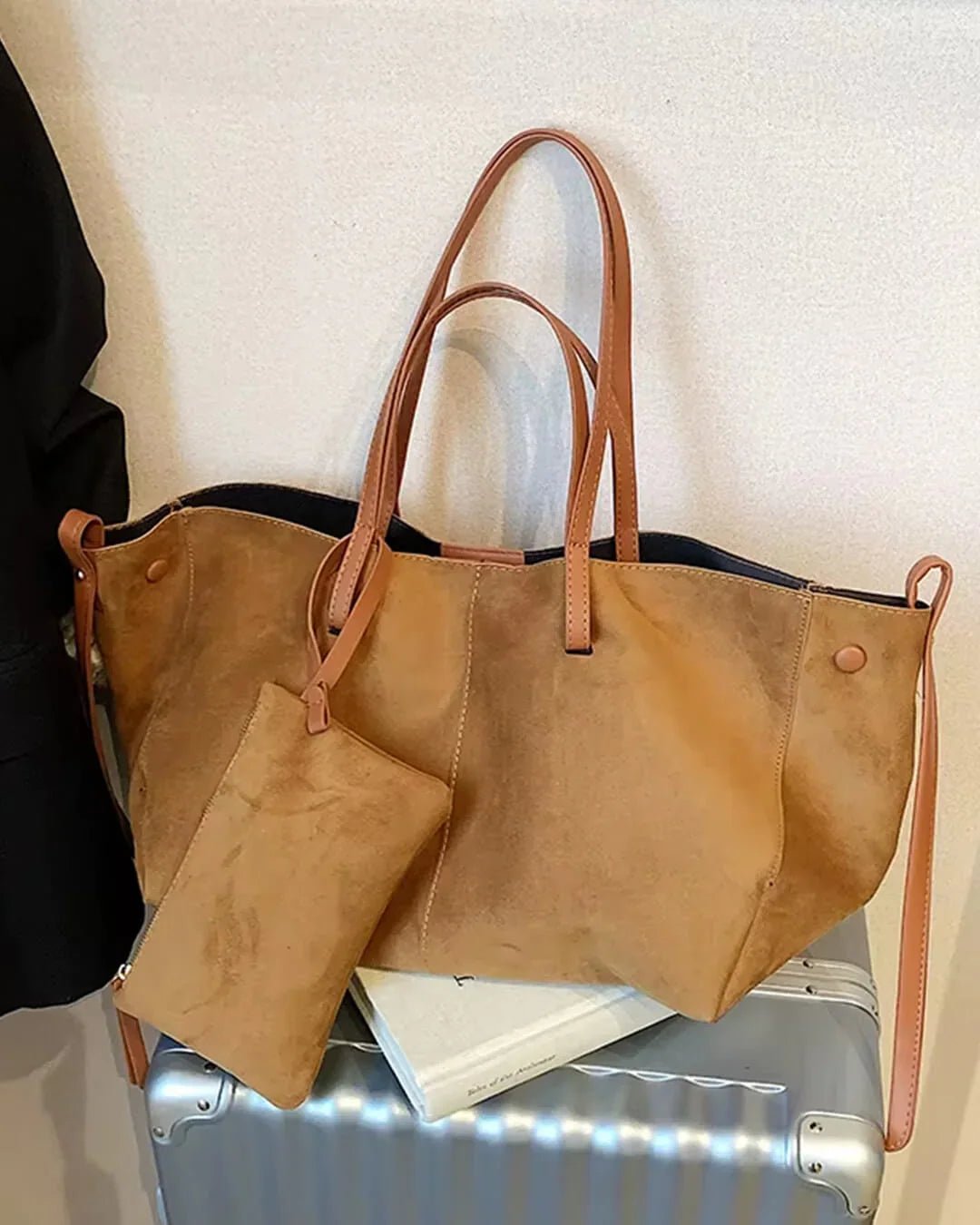 Dark brown suede tote bag with tan leather handles and attached pouch on a suitcase
