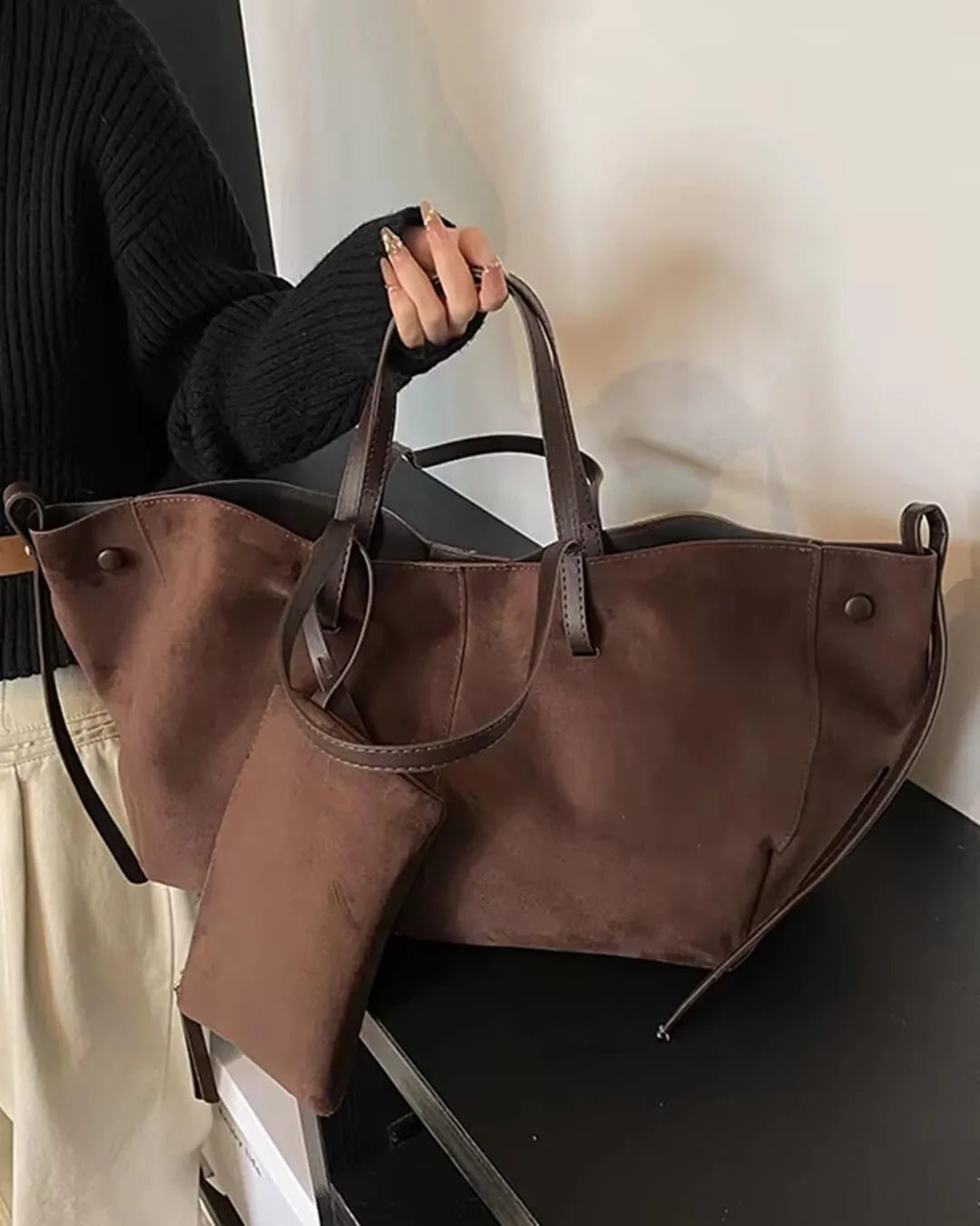 Dark brown suede tote bag with matching pouch, held by woman in black sweater