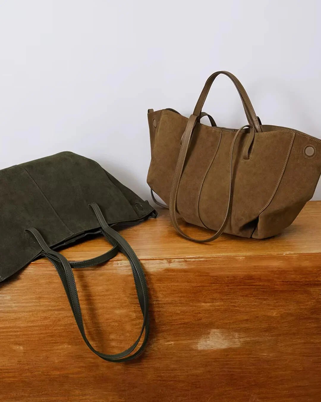 Khaki suede tote bags with leather handles on wooden surface, minimalist style.