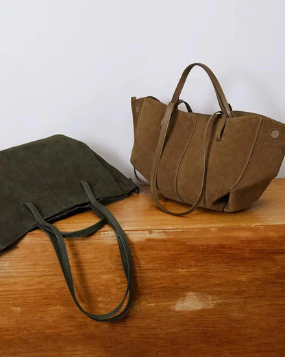 Khaki suede tote bags with leather handles on wooden surface, minimalist style.