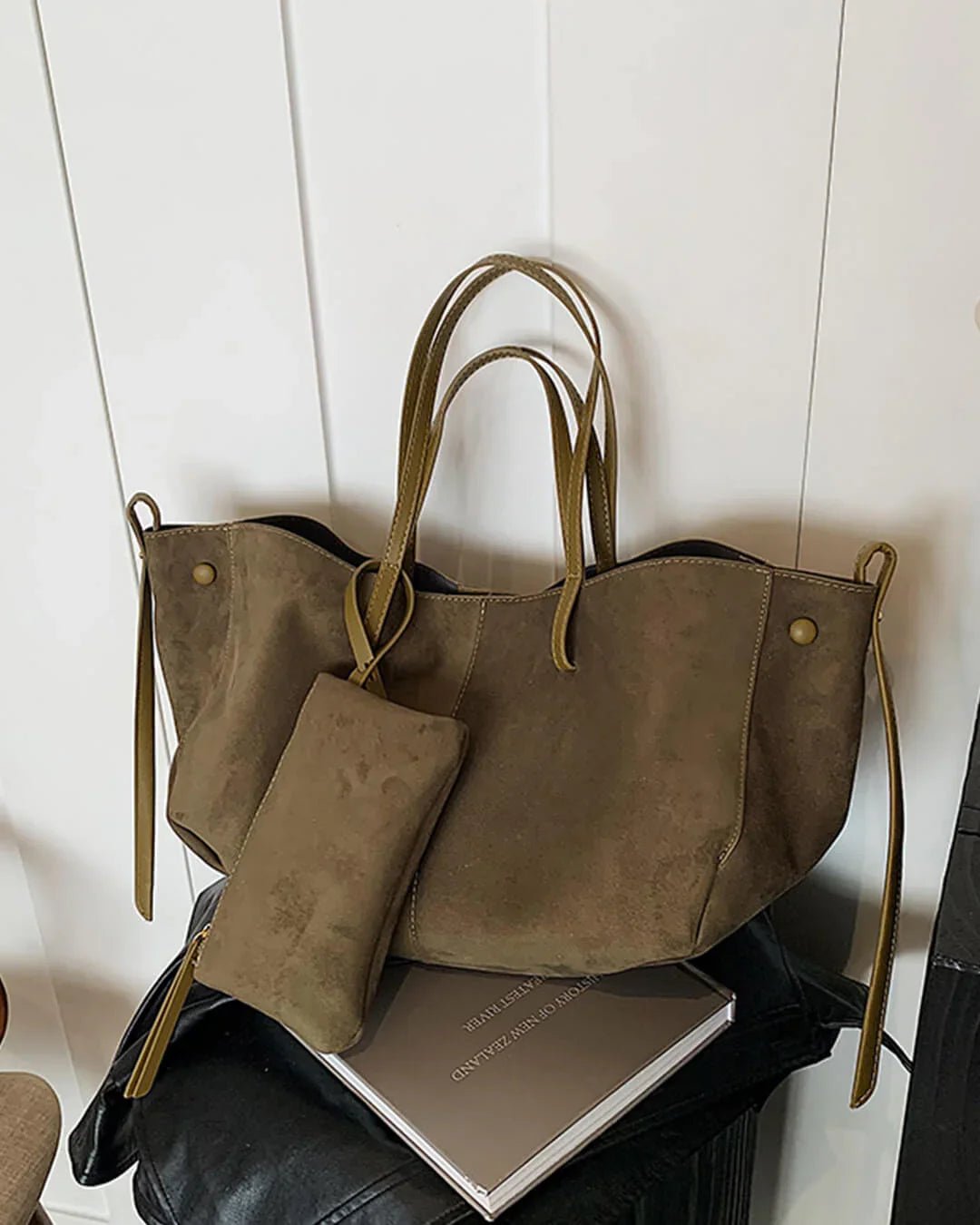 Khaki suede tote bag with matching pouch, double handles, and gold rivet accents on white wall.