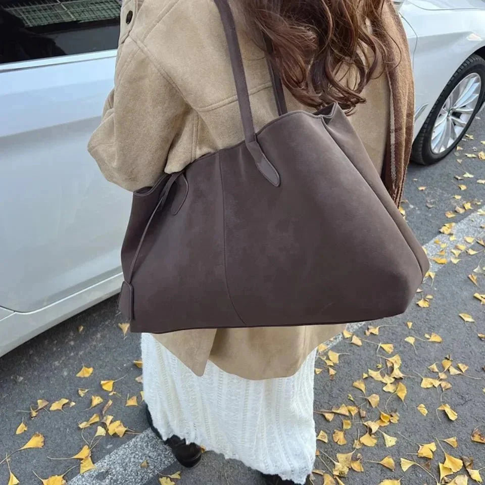 Woman holding large brown vegan suede handbag in retro style on autumn street