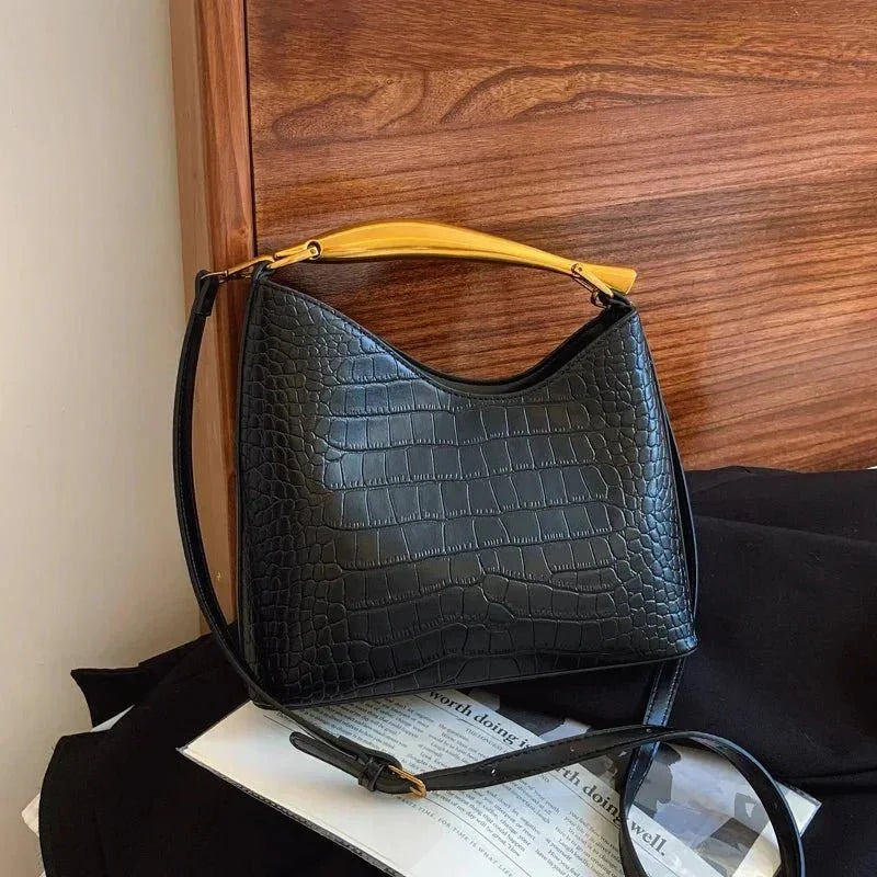 Black crocodile pattern handbag with tan top handle and adjustable shoulder strap on a bed