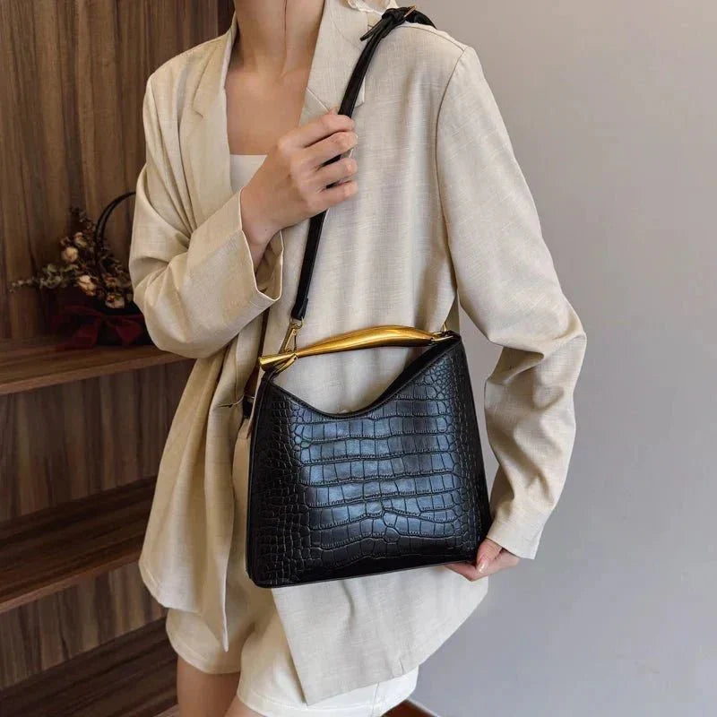 Woman holding a black crocodile pattern handbag with gold handle and top strap
