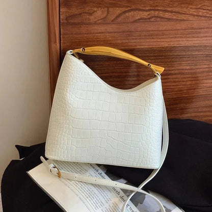White crocodile pattern handbag with yellow handle and crossbody strap on a wooden background