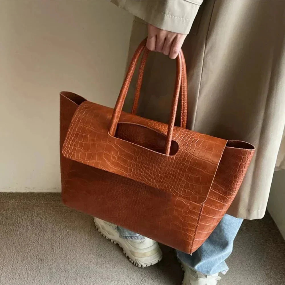 Woman holding large dark brown crocodile pattern tote handbag with double handles
